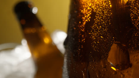 Nahaufnahme-Von-Kondensationstropfen,-Die-An-Glasflaschen-Mit-Kaltem-Bier-Oder-Alkoholfreien-Getränken-Herunterlaufen,-Die-In-Einem-Mit-Eis-Gefüllten-Eimer-Vor-Gelbem-Hintergrund-Gekühlt-Werden-1